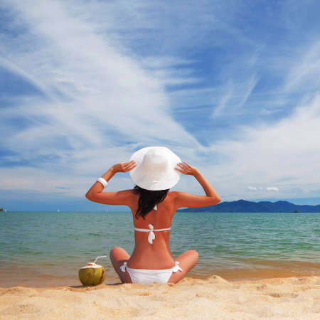 Young fashion woman relax on the beach with coconut. Happy lifestyle. White sand, blue sky and crystal sea of tropical beach. Vacation at Paradise. Ocean beach relax, travel to islandsの写真素材