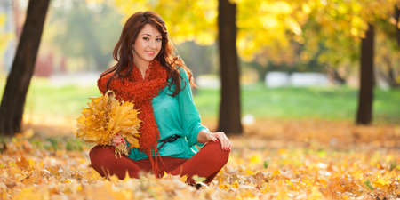 Young pretty woman relaxing in the sunny autumn park. Beauty nature scene with colorful foliage background, yellow trees and leaves at fall season. Autumn outdoor lifestyleの写真素材