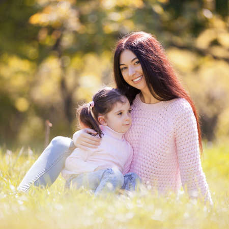 Happy mother and daughter in the autumn park. Beauty nature scene with family outdoor lifestyle. Happy family resting together on grass, having fun outdoor. Happiness and harmony in family lifeの写真素材