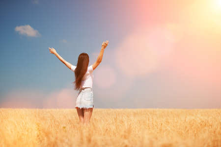Happy woman enjoying the life in the field Nature beauty, blue sky, bright sun and field with golden wheat. Outdoor lifestyle. Freedom concept. Woman jump in summer fieldの写真素材
