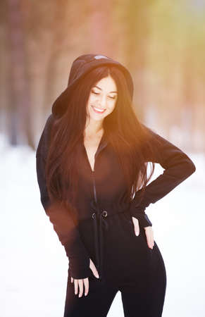 Portrait of beautiful happy stylish woman in overalls, walking at winter forest. Fashion woman lifestyle. Woman style, trendy outfit. Winter vacation.の写真素材