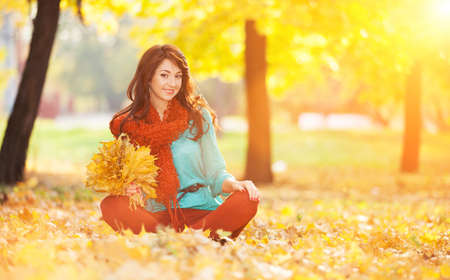 Young pretty woman relaxing in the sunny autumn park. Beauty nature scene with colorful foliage background, yellow trees and leaves at fall season. Autumn outdoor lifestyleの写真素材