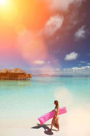 Woman walk and relax with inflatable mattress in the sea. Happy island lifestyle. White sand, crystal-blue sea of tropical beach. Vacation at Paradise. Ocean beach relax, travel to Maldives islandsの写真素材
