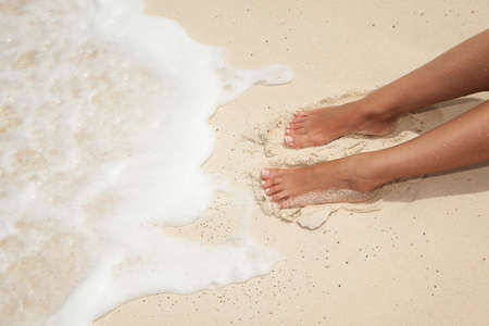 Summer beach concept. Care for beautiful woman skin and nails. Woman legs, spa therapy. Closeup photo of sandy female feet with white french pedicure on the beach background.の写真素材