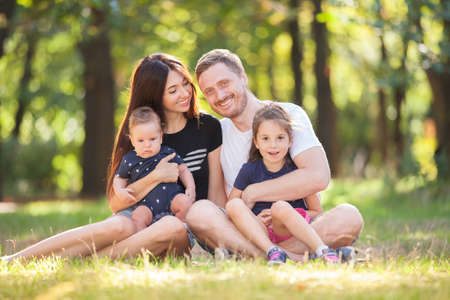 Happy mother, father, son and daughter in the park. Beauty nature scene with family outdoor lifestyle. Happy family resting together sitting on the grass, having fun outdoor. Happiness and harmony in family lifeの写真素材