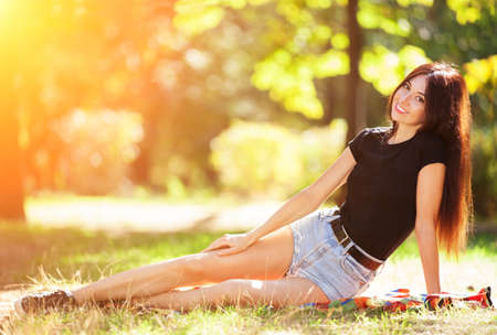 Young woman relax in the park on green grass. Beauty nature scene with colorful background, trees at autumn season. Outdoor lifestyle. Happy smiling woman sitting on green grassの写真素材