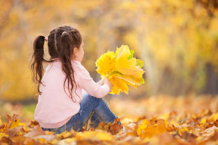 Happy girl playing yellow leaves in the autumn park. Beauty nature scene with family outdoor lifestyle. Happy girl having fun outdoor. Happiness and harmony in childhoodの写真素材