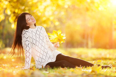 Young pretty woman relaxing in the sunny autumn park. Beauty nature scene with colorful foliage background, yellow trees and leaves at fall season. Autumn outdoor lifestyleの写真素材