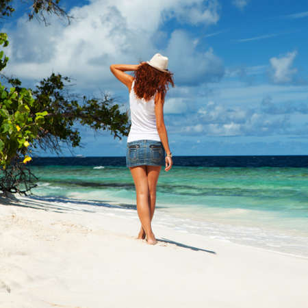 Fashion woman walking on the beach. Happy island lifestyle. White sand, blue cloudy sky and crystal sea of tropical beach. Vacation at Paradise. Ocean beach relax, travel to Maldives islandsの写真素材