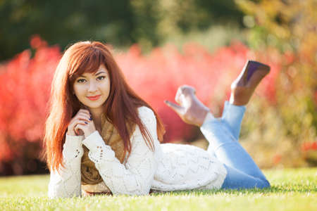 Young woman walking in the park. Beauty nature scene with colorful background, trees and leaves at fall season. Autumn outdoor lifestyle. Happy smiling woman relax on green grassの写真素材