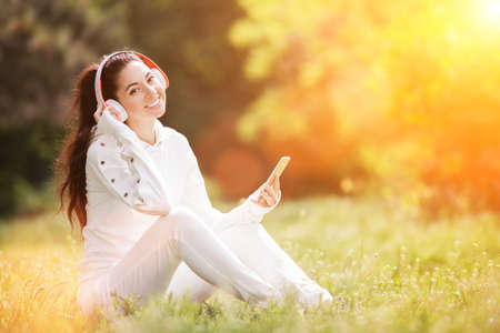 Happy woman with headphones relaxing in the autumn park. Beauty nature scene with colorful background. Fashion woman enjoying the music from her mobile phone at fall. Outdoor lifestyleの写真素材