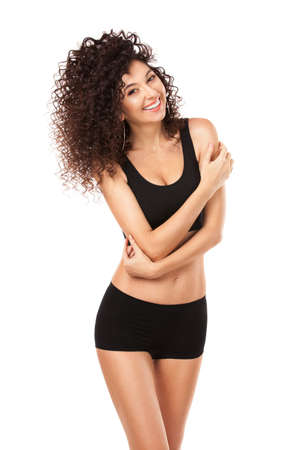 Sexy sportive tanned woman with an afro hairstyle smiling on white background. Portrait of brunette girl with long curly hair in lingerie. Model woman with wavy hairstyle and fitness body.の写真素材