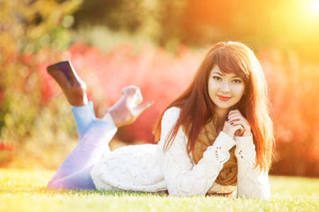 Young woman walking in the park. Beauty nature scene with colorful background, trees and leaves at fall season. Autumn outdoor lifestyle. Happy smiling woman relax on green grassの写真素材