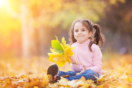 Happy girl playing yellow leaves in the autumn park. Beauty nature scene with family outdoor lifestyle. Happy girl having fun outdoor. Happiness and harmony in childhoodの写真素材