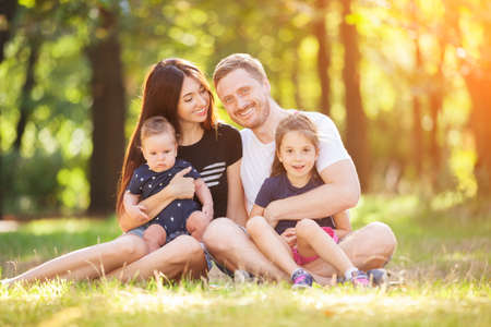 Happy mother, father, son and daughter in the park. Beauty nature scene with family outdoor lifestyle. Happy family resting together sitting on the grass, having fun outdoor. Happiness and harmony in family lifeの写真素材