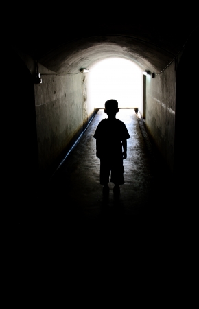 young boy in long tunnel walkway with the white light at the endの写真素材