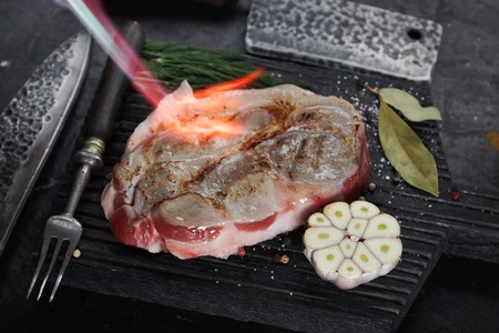 Fried meat on a wooden board with metal cookware on dark stone backgroundの写真素材