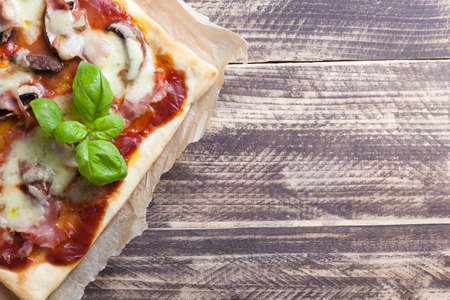 pizza slice prosciutto funghi ham mushrooms with basil leafs on vintage woodの写真素材
