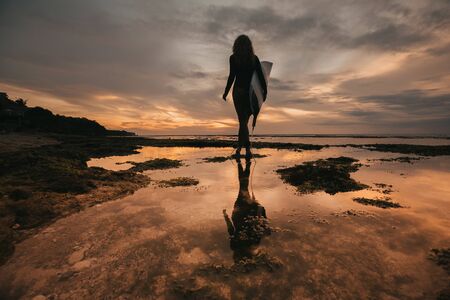 surf girl meets sunset on the beach. silhouetteの写真素材