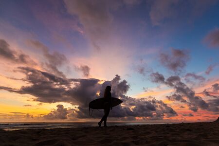 surf girl meets sunset on the beach. silhouetteの写真素材