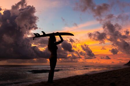 surf girl meets sunset on the beach. silhouetteの写真素材