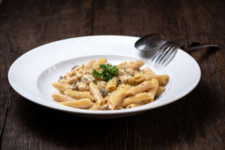 Penne pasta with white mushrooms porcini in creamy sauce on the dark wood tableの写真素材