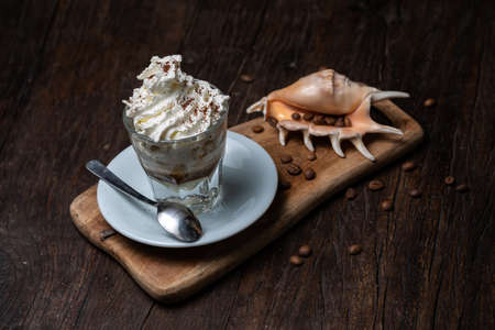 Ice Cream with vanilla coffee, Affogato al Caffe. Coffee Frappe Galao macchiato with shell on the dark old wooden table. Coffee beans. Glass on the white plate. Irish coffee, cafe au lait, cortadoの写真素材