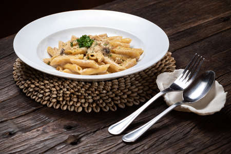 Penne pasta with white mushrooms porcini in creamy sauce on the dark wood tableの写真素材