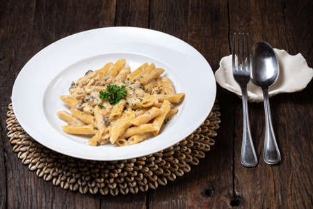 Penne pasta with white mushrooms porcini in creamy sauce on the dark wood tableの写真素材