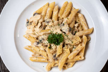 Penne pasta with white mushrooms porcini in creamy sauce on the dark wood tableの写真素材