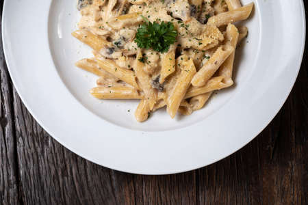 Penne pasta with white mushrooms porcini in creamy sauce on the dark wood tableの写真素材