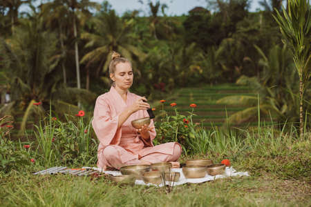 Blonde woman in a pink kimono playing on meditative Himalayan singing bowl.の写真素材