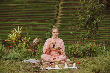 Blonde woman in a pink kimono playing on meditative Himalayan singing bowl.の写真素材