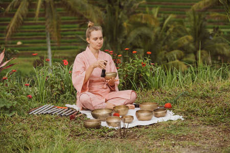 Blonde woman in a pink kimono playing on meditative Himalayan singing bowl.の写真素材