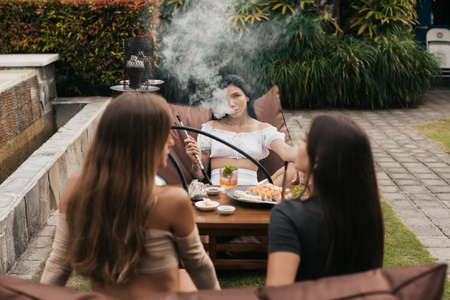 Group of young women with dark hair smoking a hookah and exhaling white smoke.の写真素材