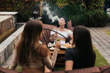 Group of young women with dark hair smoking a hookah and exhaling white smoke.の写真素材