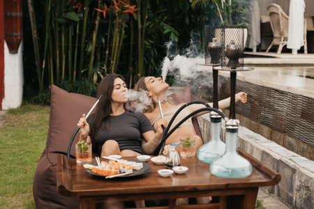 Group of young girls smoking a hookah and exhaling white smoke. Vacation.の写真素材