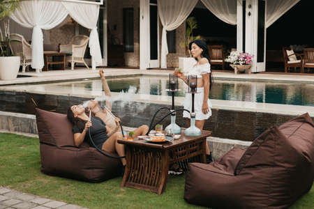 Group of young women with dark hair smoking a hookah and exhaling white smoke.の写真素材