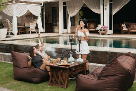 Group of young women with dark hair smoking a hookah and exhaling white smoke.の写真素材