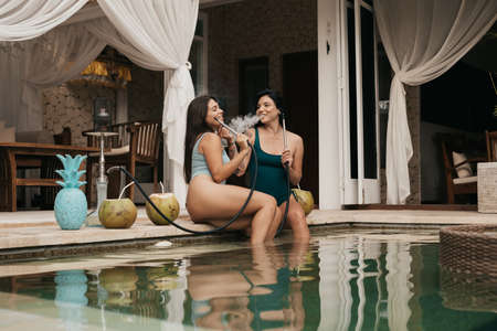 Group of young girls with dark hair in bikini smoking a hookah or shishaの写真素材