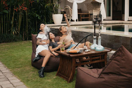 Group of young women with dark hair smoking a hookah and exhaling white smoke.の写真素材