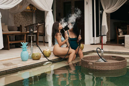 Group of young girls with dark hair in bikini smoking a hookah or shishaの写真素材