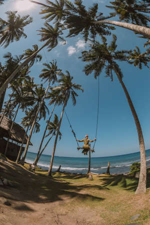 Young women in green dress swinging over the beach near the oceanの写真素材