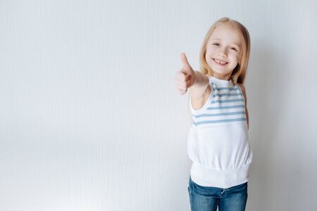 Portrait of a beautiful and laughing blonde little girl showing thumbs up isolated one white...