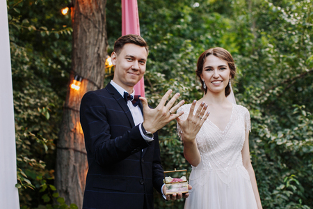 Happy family of groom and bride at wedding day ceremory with arch and retro lightbulb on background shows their hands with rings. Smiling newlyweds together. Concept of love and happinessの写真素材