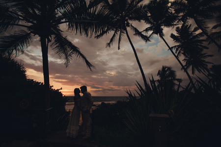 Two young lovers standing on a beach and looking to each other on sunset palm trees background.silhouette couple loveの写真素材