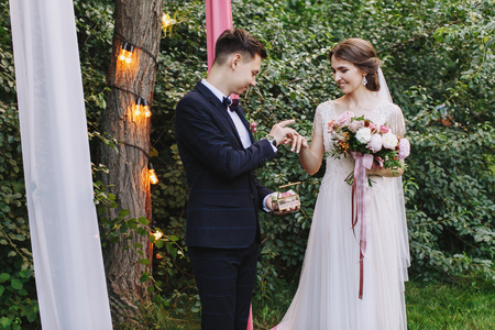 The bride and groom exchange rings during a wedding ceremony, a wedding in the summer green garden with retro bulbs.gorgeous bouquetの写真素材