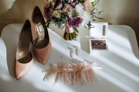 Bridal morning details composition. Top view of wedding rings, beautiful bouquet of violet flowers with ribbons, earrings, garter and leather shoes. Flat lay.の写真素材