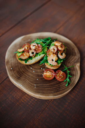 Tasty snack of open sandwich with avocado, shrimps and arugula on wooden cutting board. Top...