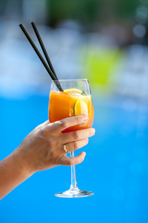 Woman holds orange cocktail on swimming pool backgroundの写真素材